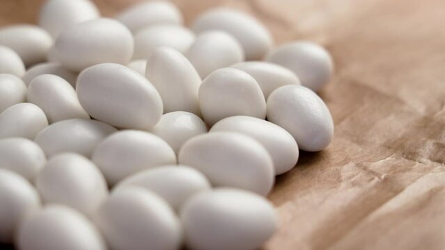 White chocolate covered almond nuts on wrapping pack paper. Yummy crunchy natural candies or dragee. Rotation