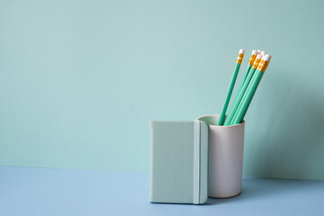 Pencil holder and diary notebook on blue desk. mint green background