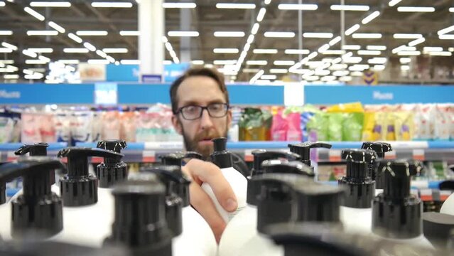 Many plastic bottles with liquid soap or shower gel in a hypermarket and a buyer takes one