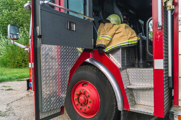 The open door of the fire truck cabin where the firefighters are located. A firefighter's protective clothing is in the cabin of a fire truck. Helmet and boots of a firefighter in a fire truck.