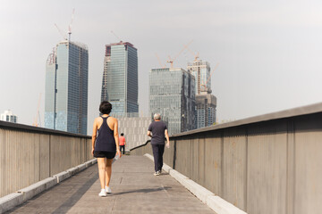 Woman exercise walking on the bridge hand holding bottle water with city building view.