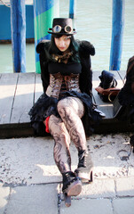 Steampunk girl in stockings, dress, corset, top hat, and retrofuturistic glasses poses in Venice...