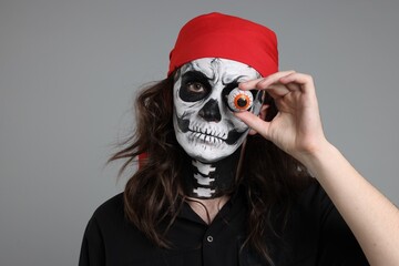 Man in scary pirate costume with skull makeup and decorative eyeball on light grey background....