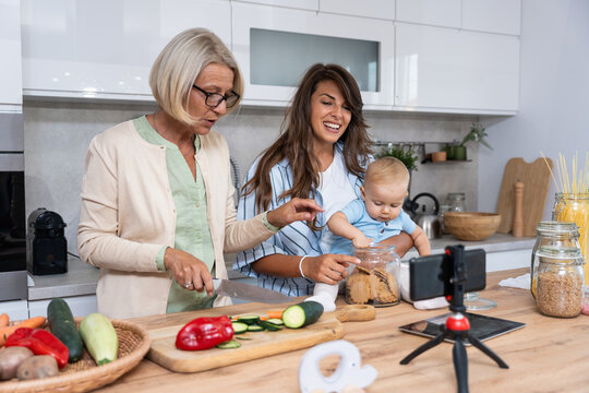 Grandmother daughter, mother and baby, grandchild cooking together in domestic kitchen, happy family while talking on video call over smartphone with child father who working as military man