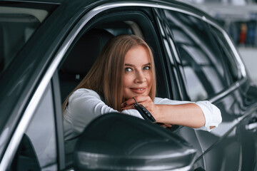 Looking from the opened window. Woman is sitting in a car and driving it