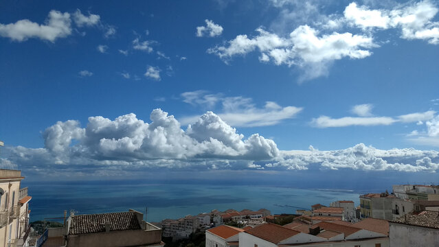 Cloudy sky over Manfredonia Gulf, Puglia. In the foreground, Monte Sant'Angelo's medieval houses on a hill. Romantic view with glimpses of the blue sea through clouds.