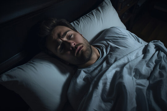 A man with a stressed expression lies in bed due to insomnia