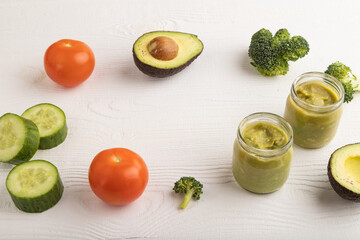 Baby puree with vegetable mix, broccoli, avocado in glass jar on white wooden, side view, copy space