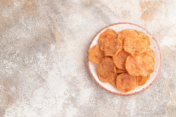 Slices of dehydrated salted meat chips on gray concrete, top view, copy space