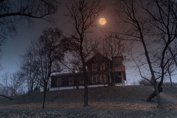 Gloomy Halloween landscape with a house and the moon and one fire in the window.