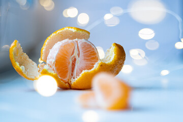 Juicy, fresh, peeled tangerine and garland lights in the background. Bokeh of garlands in the background, and in the foreground is a peeled tangerine.