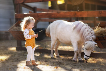 a small beautiful girl stands next to a white pony