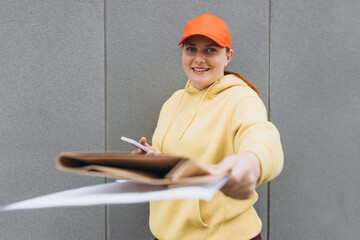 Happy 30s delivery woman in red hat with smartphone giving packages. Concept of fast delivery