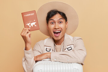 Young traveler is happy to get visa, showing his passport with smile and packed suitcase next to...