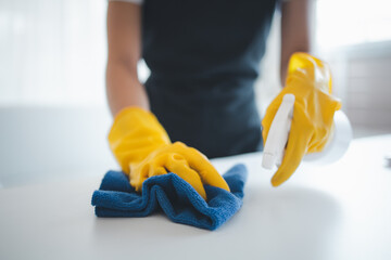 Cleaning desk surface in office with sanitizer spray, wear gloves and wipe the table with a towel, the housekeeper is cleaning the work desk for hygiene because of the Covid-19, cleaning idea.