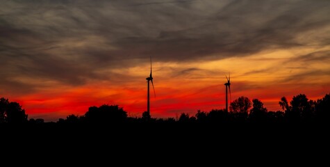 the sun rises behind the wind turbines in a red sky