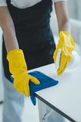 Cleaning desk surface in office with sanitizer spray, wear gloves and wipe the table with a towel, the housekeeper is cleaning the work desk for hygiene because of the Covid-19, cleaning idea.