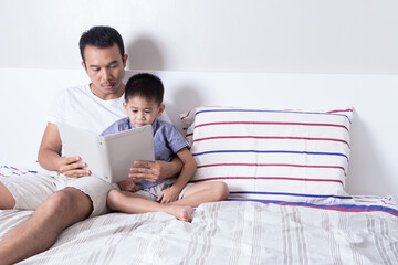 happy asian Father and son reading book together while laying on bed. happy family, father day