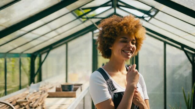 Portrait of smiling woman with garden tool working in greenhouse at home - shot in slow motion