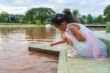 Side view little girl feeding koi carp nearby the pond.
