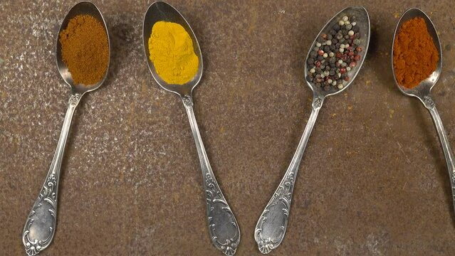 Old cupronickel spoons with various spices lie on an old metal table with traces of rust