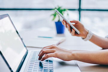 Anonymous woman in casual clothing working with blank screen laptop and smartphone at office