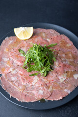 Marbled beef carpaccio with arugula, parmesan cheese, olive oil and lemon. A traditional classic appetizer made from thinly sliced raw meat. Close-up, selective focus, black background.