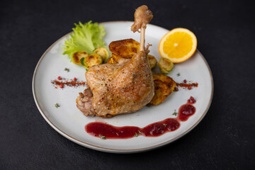Duck leg confit with Brussels sprouts, baked potatoes, thyme, orange and lingonberry sauce. Traditional French cuisine. Selective focus, close-up, black background.