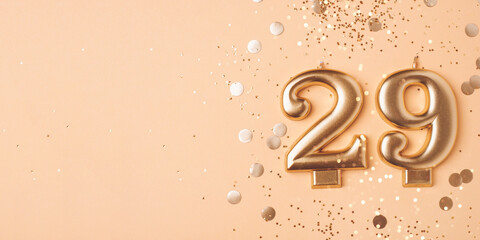 29 years celebration. Greeting banner. Gold candles in the form of number twenty nine on peach background with confetti.