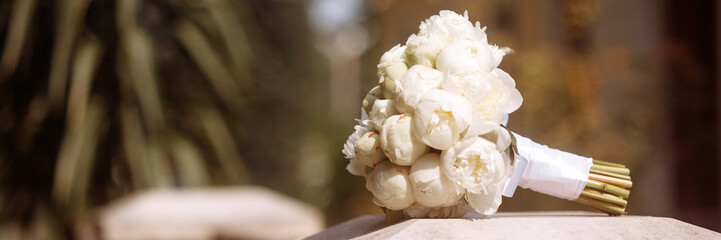 Elegant white rose bouquet on stone pillar in garden. Concept for wedding or anniversary celebration, or romantic gift. Roses symbolize purity and love. Banner with copy space.