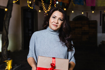 Hispanic young woman portrait holding a gif box at traditional posada party for Christmas in Mexico...