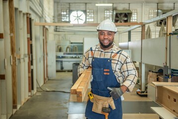 Portrait of Young black skin carpenter finished creating smiles to camera. Happy Carpenter holds wooden planks for build furniture in carpentry workshop. foreman carpenter standing in shop.