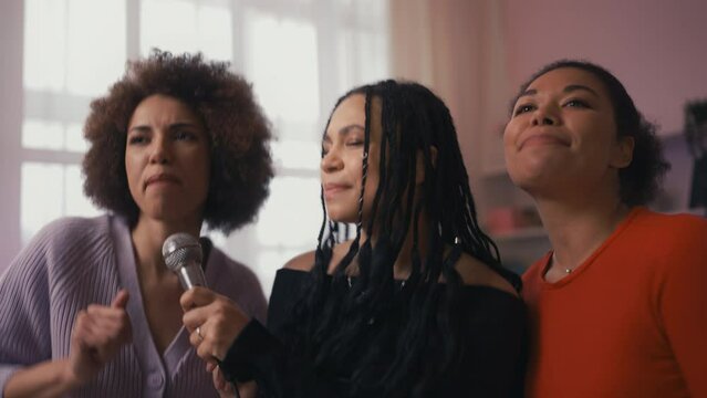 Stylish young women singing karaoke and dancing during home party, friendship