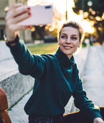 Cheerful young hipster girl with cellular phone sitting at historic urban setting