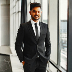 Young South Indian businessman in black suit by the window in a modern building