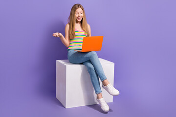 Full size photo of pretty teenager blonde girl sit cube video call netbook wear trendy striped outfit isolated on purple color background