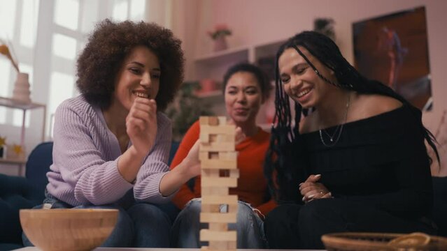 Three cheerful women friends enjoying leaning tower game at home party, fun