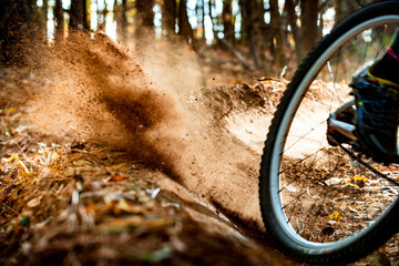 The rear tire of a mountain bike kicks up dirt along a trail in the woods