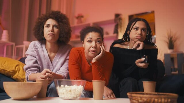 Three relaxed women friends watching boring TV show and eating popcorn, pastime