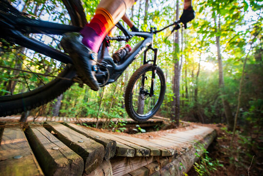 A mountain biker passes over a wooden boardwalk trail in the woods, motion blur