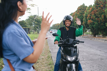 Young male online motorcycle taxi driver waving hand passenger and ready to pick up