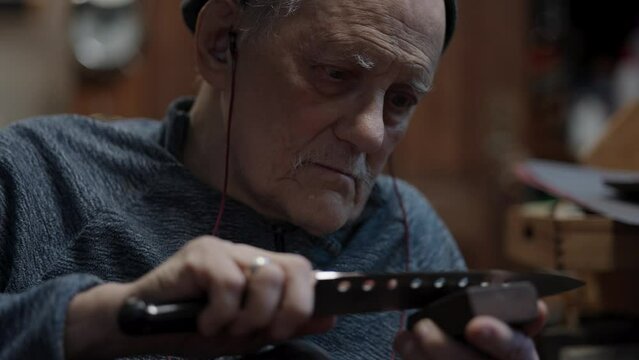 Senior gray haired male master in a wheelchair working at his workshop sharpening Japanese kitchen knife