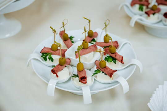 Appetizer on a plate, table setting for an event, ham and cheese on a skewer, pitted olive, catering for departure, beautiful serving of the dish.