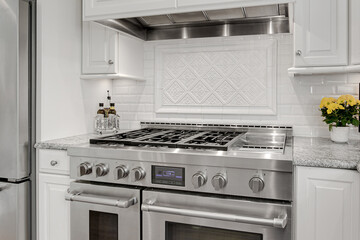 Modern Kitchen Interior with Stainless Steel Gas Stove, Elegant White Cabinetry, Ornate Backsplash Design, and Fresh Yellow Flowers - Powered by Adobe
