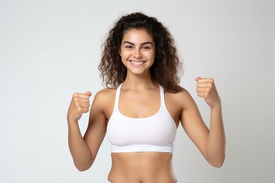 Portrait of a smiling sportswoman in white sportswear showing her thumb up and her biceps isolated on a white background and Looking at the camera.