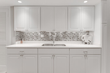 Modern White Kitchen Interior with Steel Mosaic Backsplash, Under-Cabinet Lighting, and Sleek Stainless Steel Faucet
