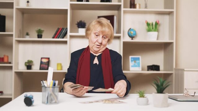 older, sad woman discontentedly counts dollar bills, arranging them on the table