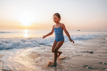 The child happily plays in the waves on the seashore. A girl in a blue swimsuit laughs while...