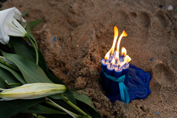 Blue candles with a lit flame and a white flower on the beach sand. Gift for Iemanja the queen of the sea.