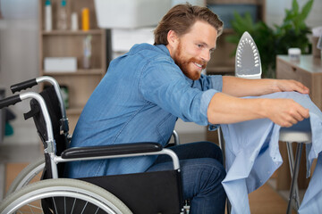 young man in wheel-chair doing ironing at home - obrazy, fototapety, plakaty